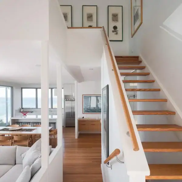 Architectural open-plan living room with timber stairs and ocean views in a coastal home by Simpson and Co Projects.