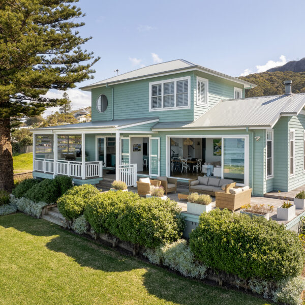 Elevated exterior view of the Wombarra No. 3 home by Simpson & Co Projects, featuring green weatherboards, white trims, lawn and surrounding coastal trees.