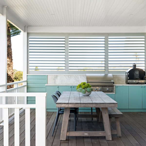 Outdoor dining area of the Wombarra No. 3 home by Simpson & Co Projects, with louvred windows, green feature wall, white trims and timber dining table.