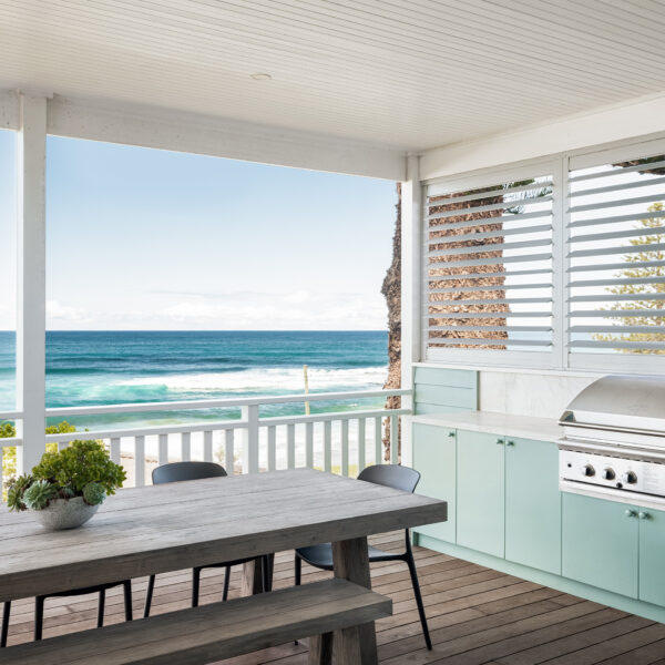 Outdoor kitchen and dining area of the Wombarra No. 3 home by Simpson & Co Projects, with green cabinetry, timber decking, louvred screening and ocean views.