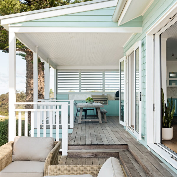 Verandah seating area of the Wombarra No. 3 home by Simpson & Co Projects, with timber decking, white trims, balustrades and green weatherboard facade.