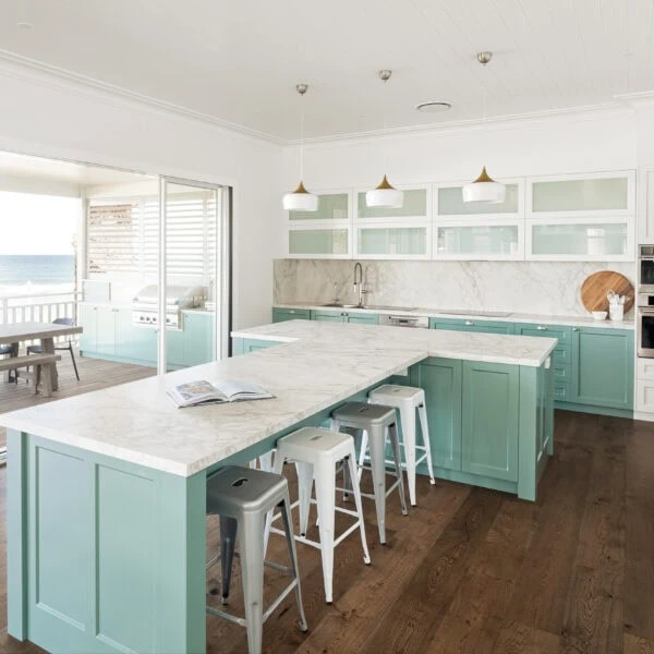 Large coastal kitchen island with marble benchtop and seating for eight, mint cabinetry and timber flooring at Wombarra No. 3.
