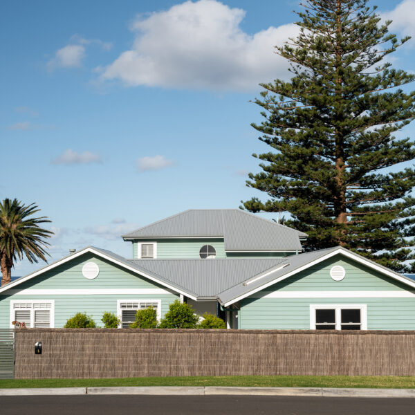 Side elevation of the Wombarra No. 3 home by Simpson & Co Projects, showing green weatherboards, white trims, walkway and ocean views.