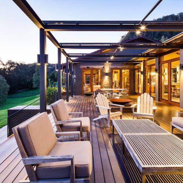 Outdoor entertaining terrace at Ooralba Estate featuring timber posts, covered pergola structure, outdoor dining furniture, and views over the surrounding Kangaroo Valley landscape at dusk.