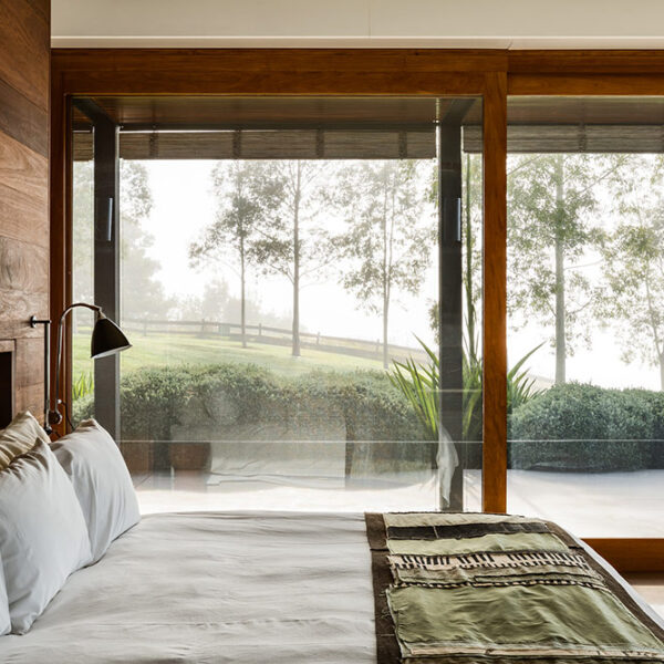 Bedroom at Ooralba Estate with timber detailing, soft neutral furnishings, and expansive glass doors opening to the Kangaroo Valley bushland.