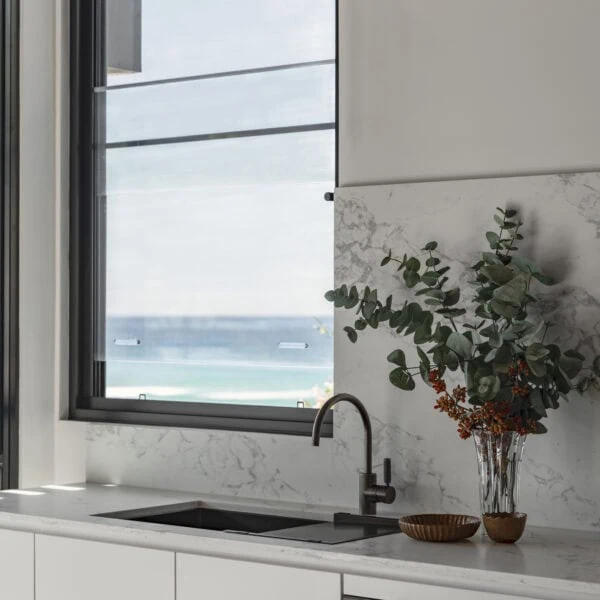 Kitchen window in Stanwell Park No.3 overlooking the coastal landscape with stone benchtop and contemporary tapware.