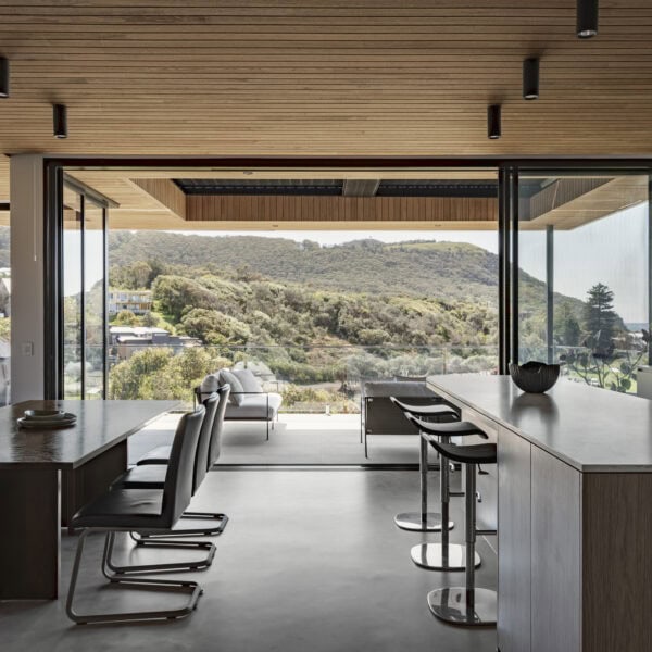 Open-plan kitchen and living area in Stanwell Park No.3 with timber ceiling, large glazing and views across the coastal landscape.