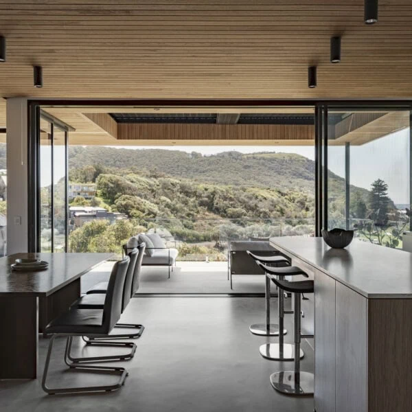 Open-plan kitchen and living area in Stanwell Park No.3 with timber ceiling, large glazing and views across the coastal landscape.